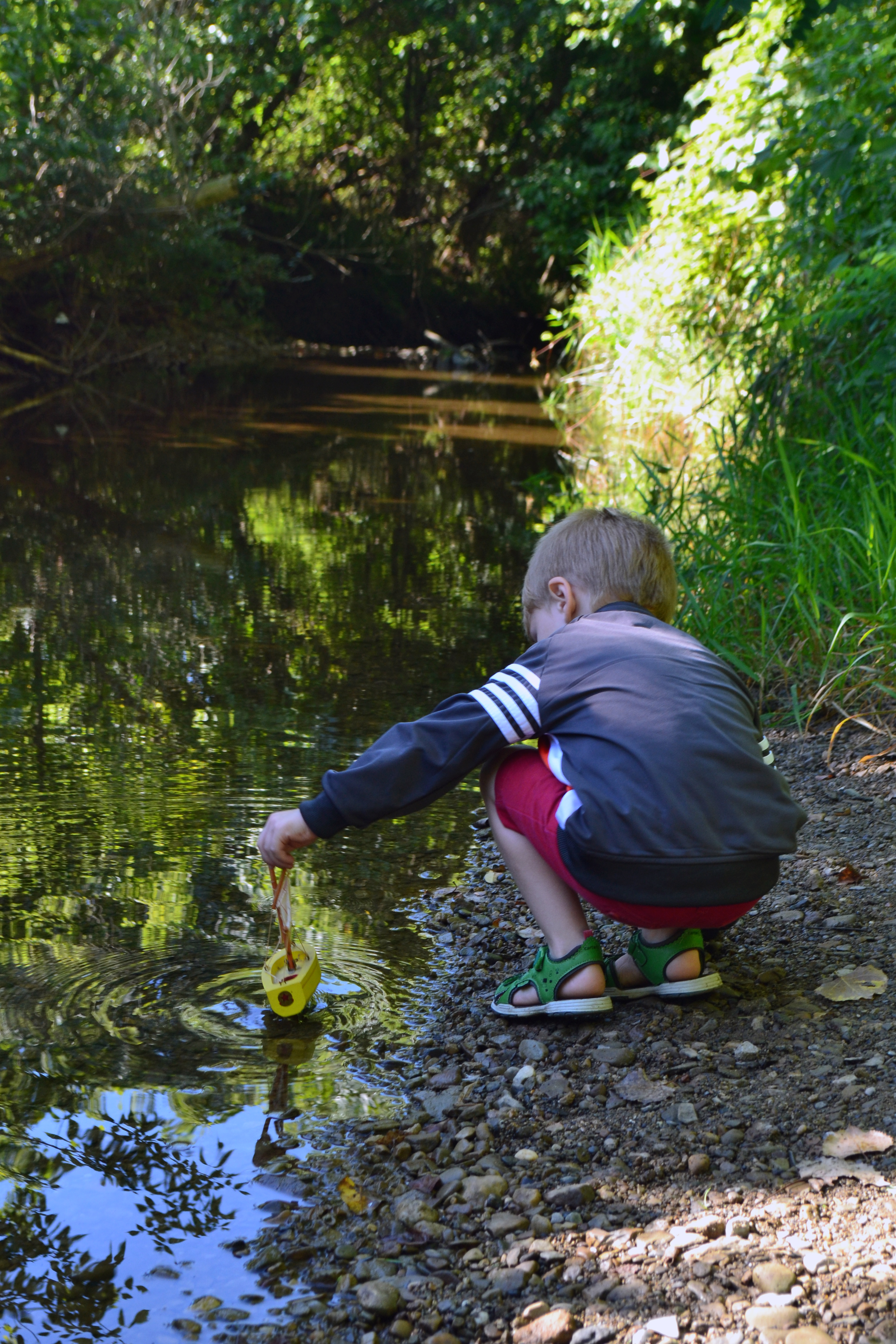child in stream with toy sailboat